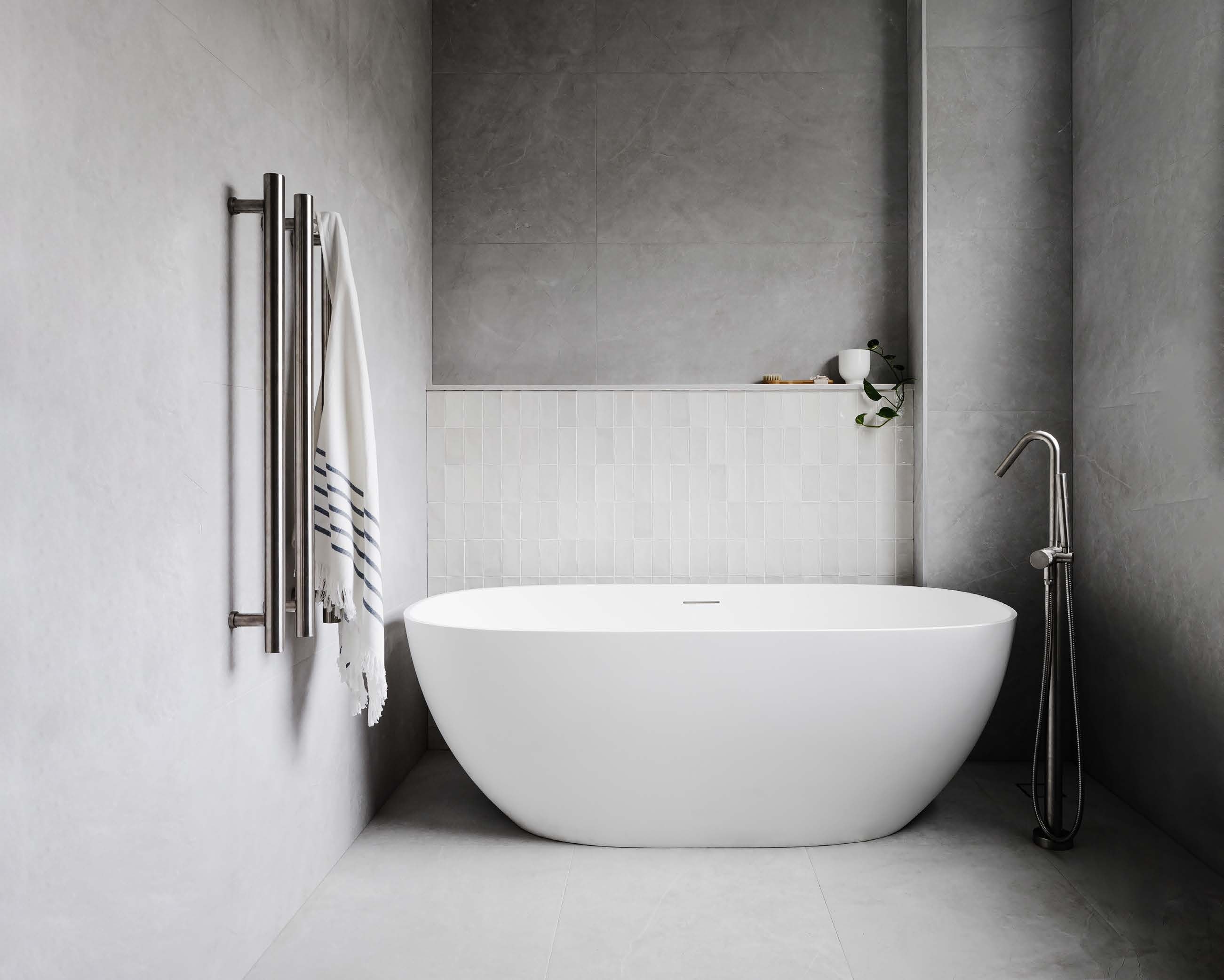 A family bathroom with a freestanding bath, large-format grey tiles and a gloss tiled feature wall