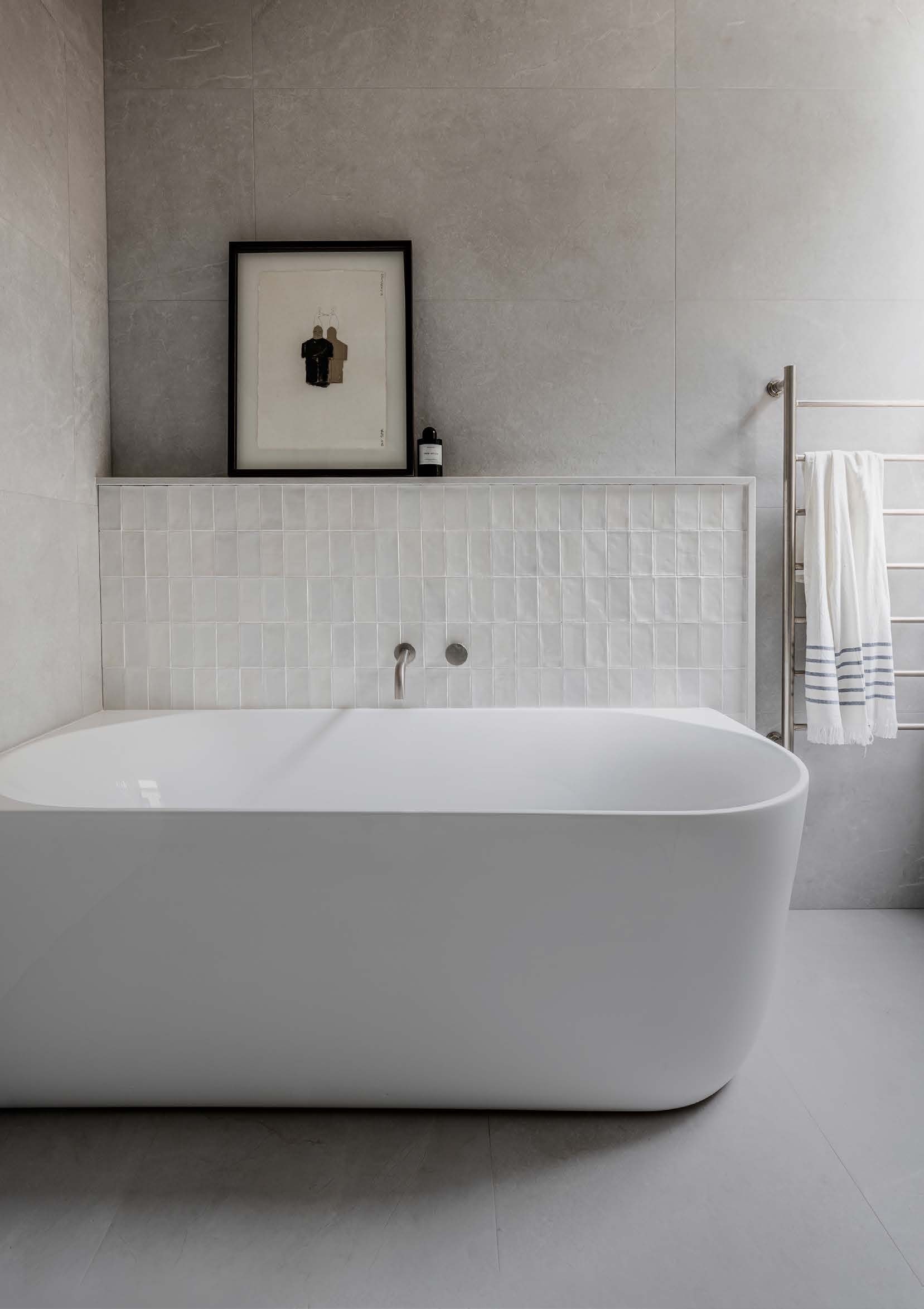 A powder room with a back-to-corner bath, a tiled nib wall and a framed artwork resting above it